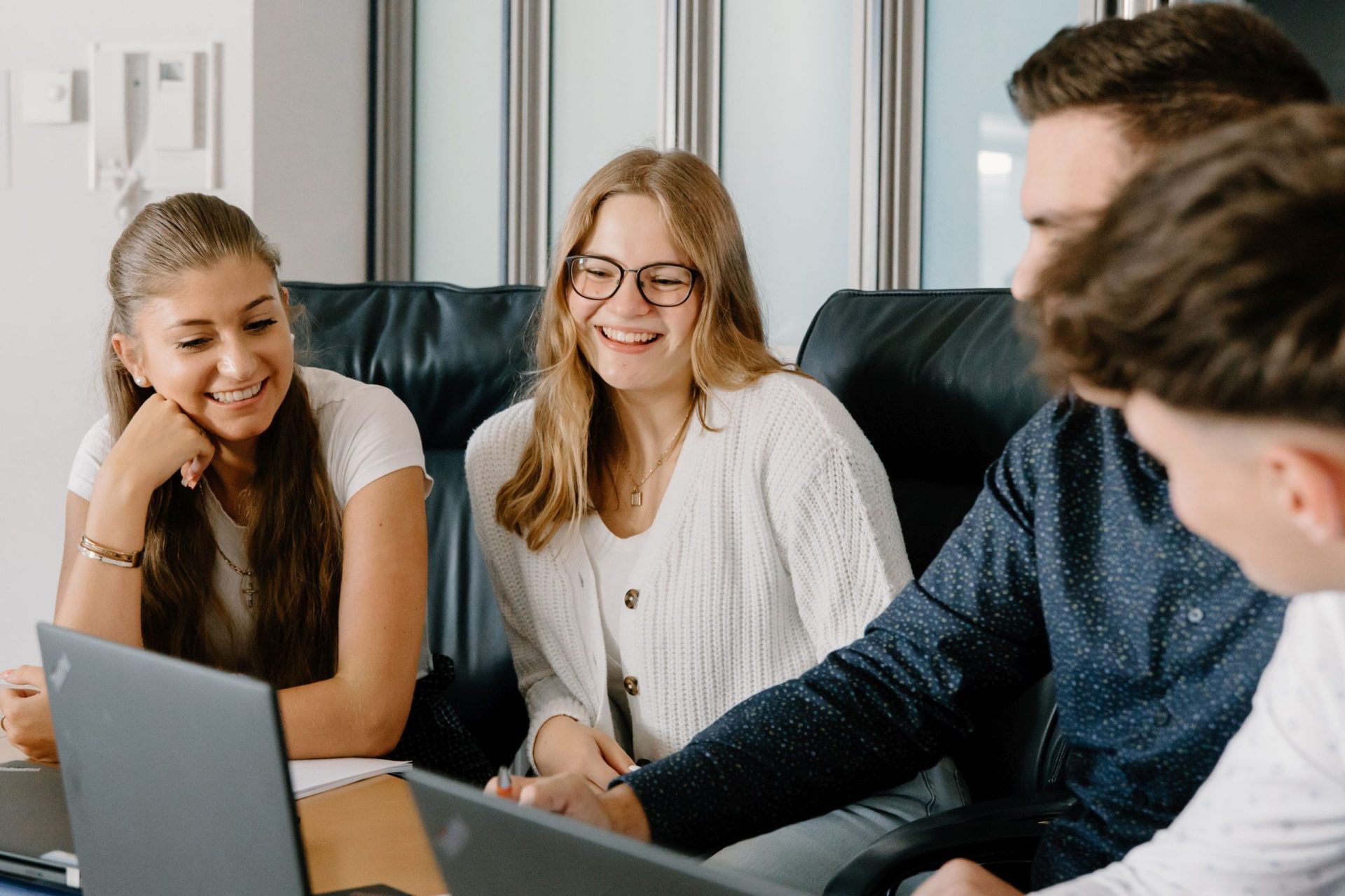 Vier junge Menschen sitzen an einem Tisch mit Laptops und lachen gemeinsam bei der Arbeit.